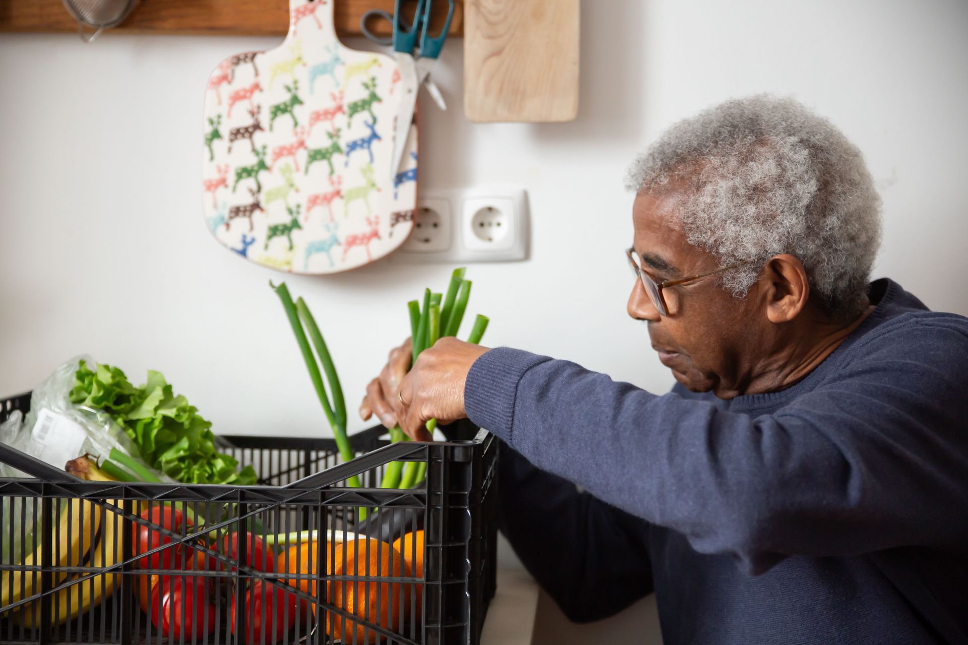 Senior African American man organizing fresh vegetables indoors, showcasing healthy lifestyle.