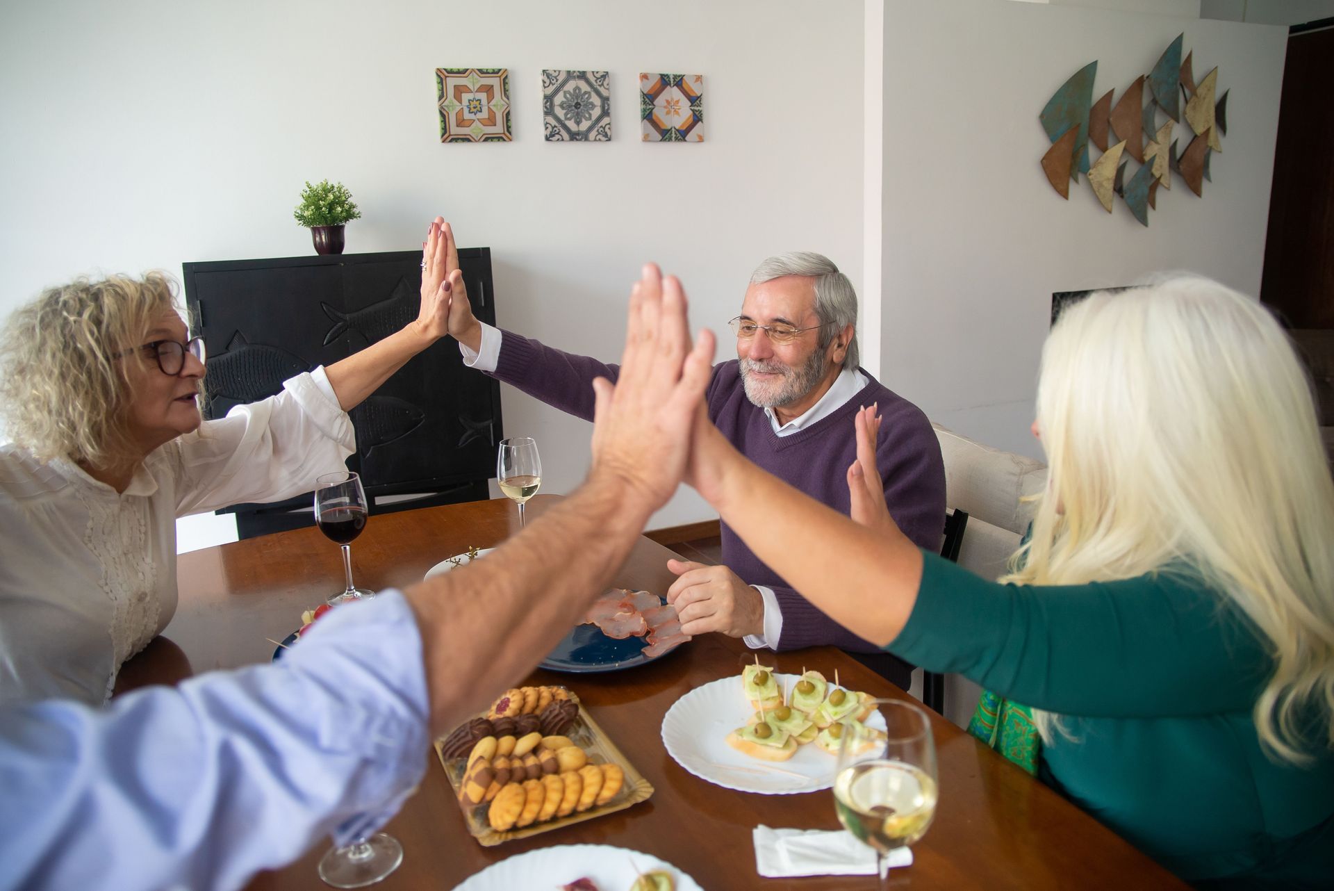 A group of senior friends enjoying dinner together, sharing a high five in a warm, friendly setting.